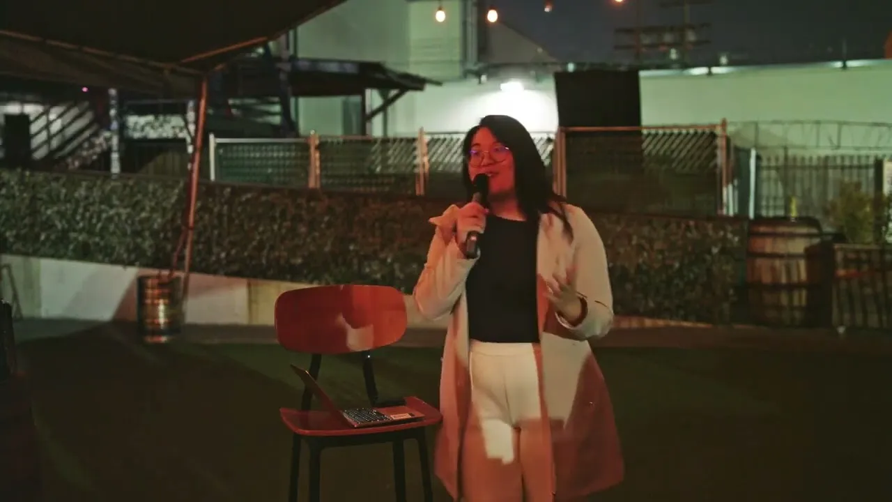 Nanavati Low speaking on an outdoor stage at night, microphone in hand.